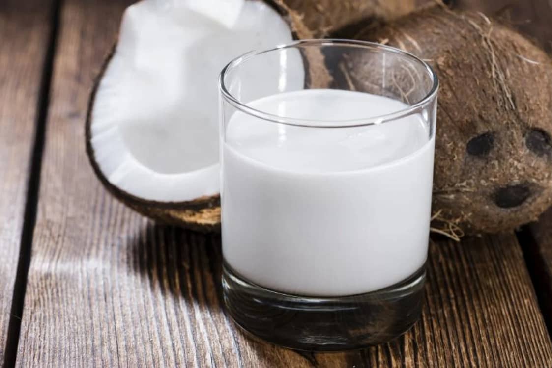 Laptele de cocos într-un pahar lângă o nucă și jumătate de cocos Foto mancarecucap
