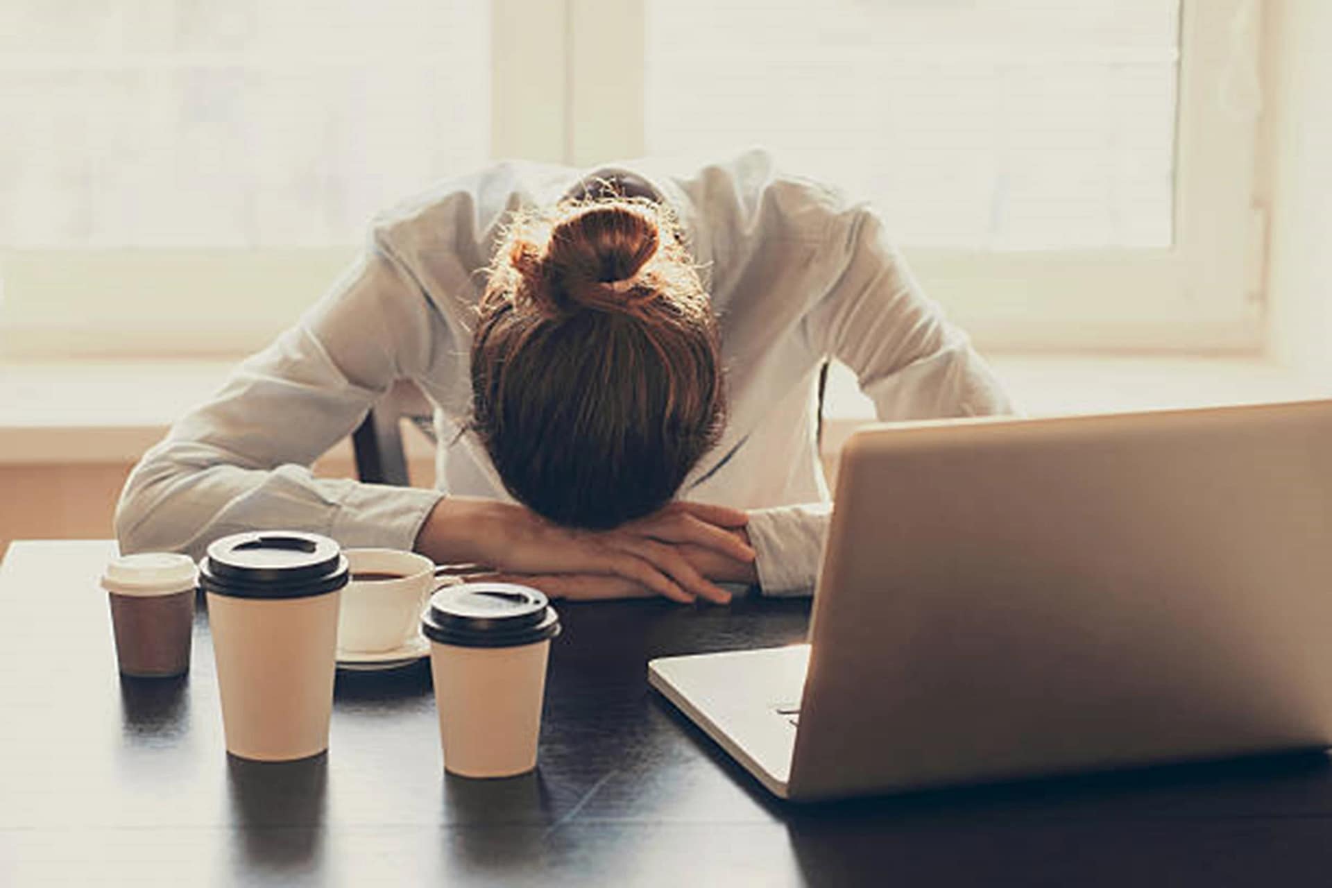 O femeie care doarme cu capul pe biroul de lucru, în ciuda paharelor de cafea băută Foto iStock